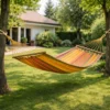 Hamac 2 places en coton rayé kaki et jaune avec barres en bois suspendu entre arbres dans jardin